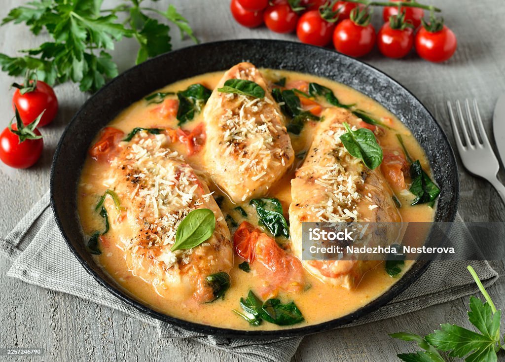 chicken breast in creamy sauce with tomatoes and spinach on plate